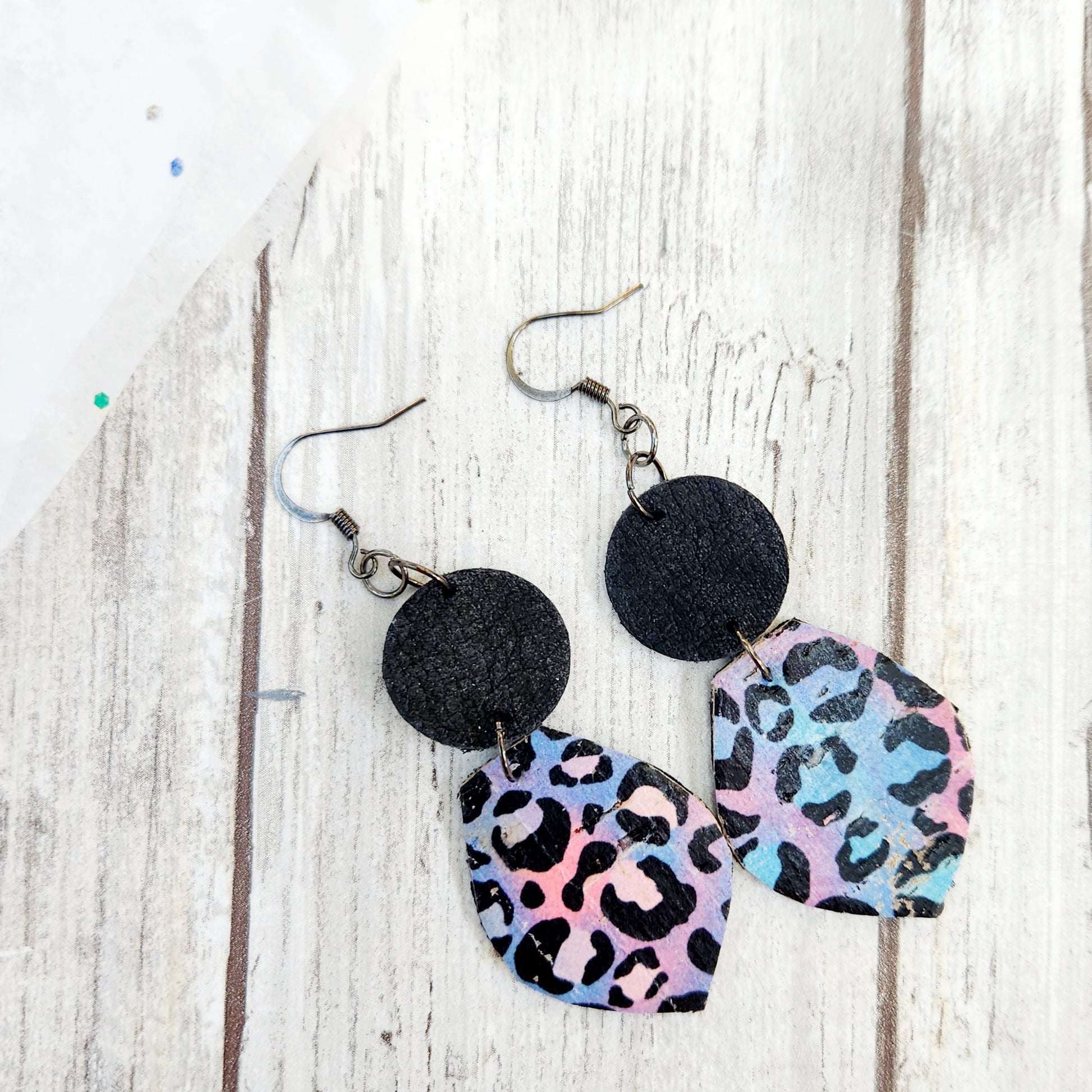Lisa, black leather circles holding up cork on leather petals with a pink, blue and purple swirled background and black leopard print. 