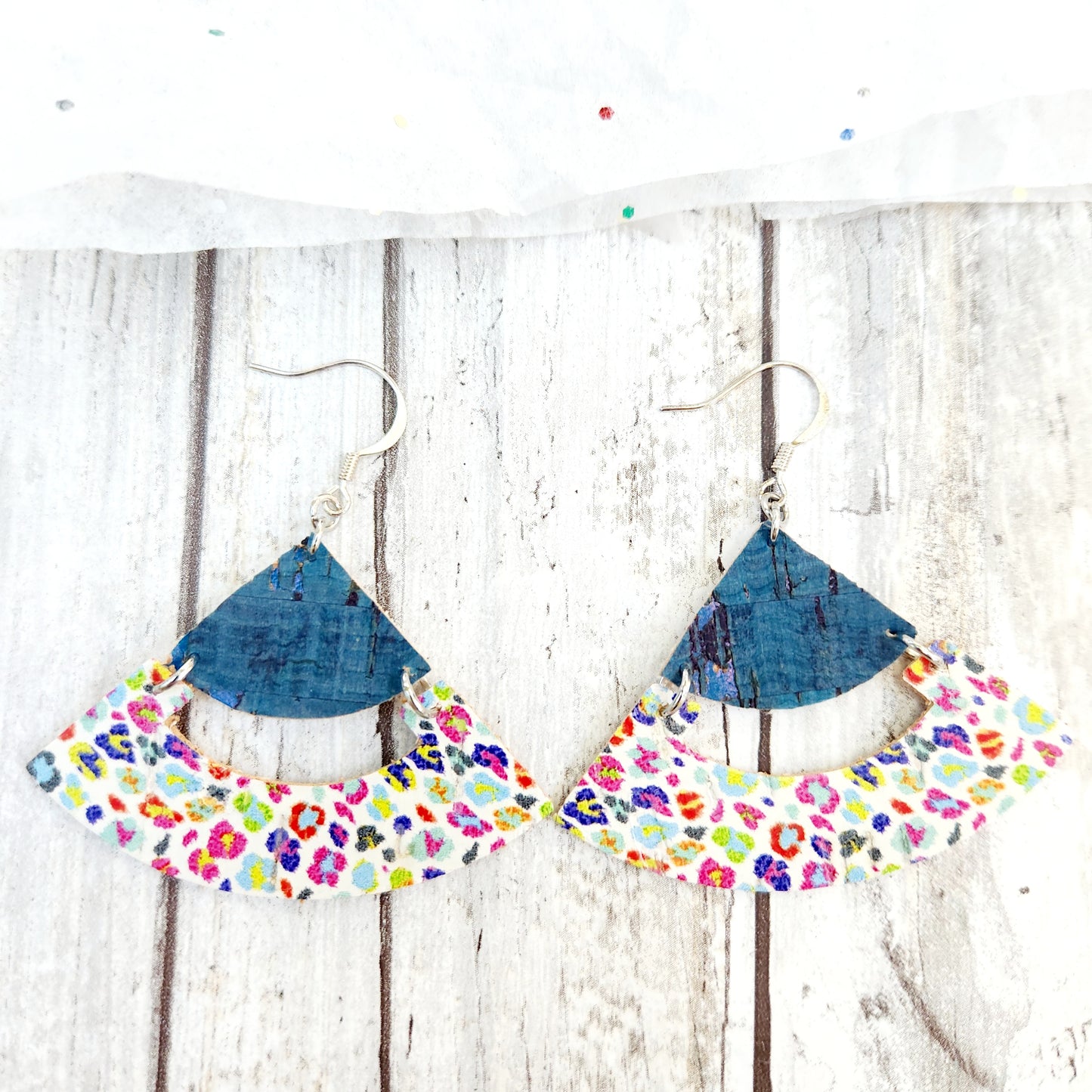 Farrah, a jpinted, rounded triangle earring, with bright teal points supporting a ehite cork with a neon leopard print on the bottom. 