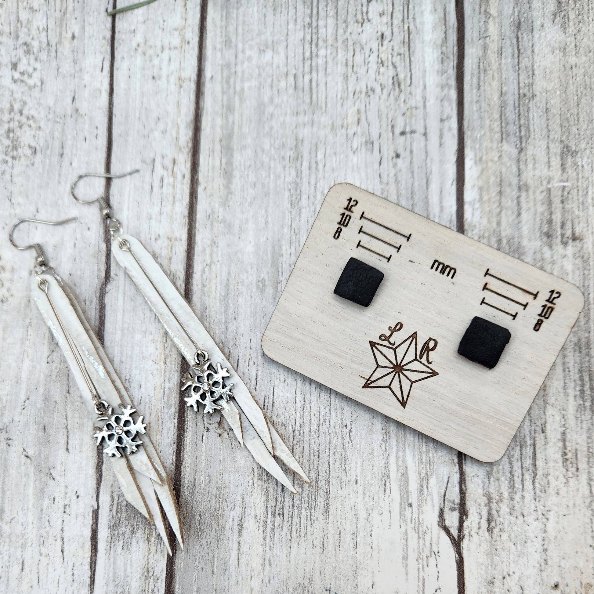 Winter earrings, Icicle has white leather with metallic silver highlights cut into angles fringe with a snowflake charm in front. With matte black Lil studs in square.