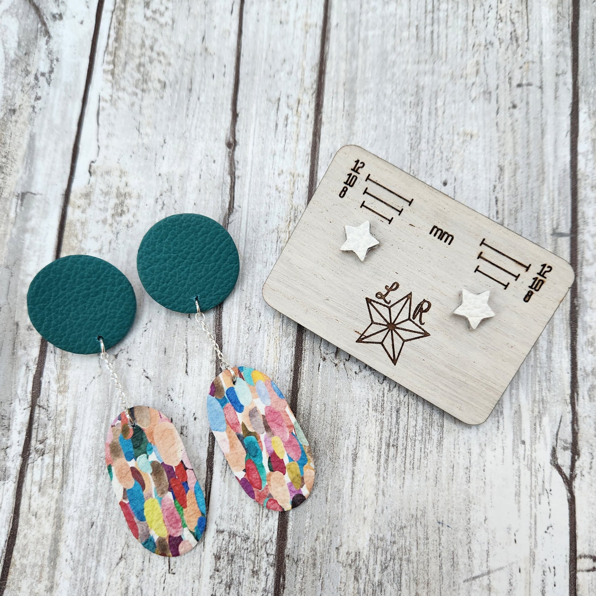 Summer themed leather earrings. Rachel has a teal leather circle and a confetti print oval hanging off it on a silver chain. With white star Lil studs.